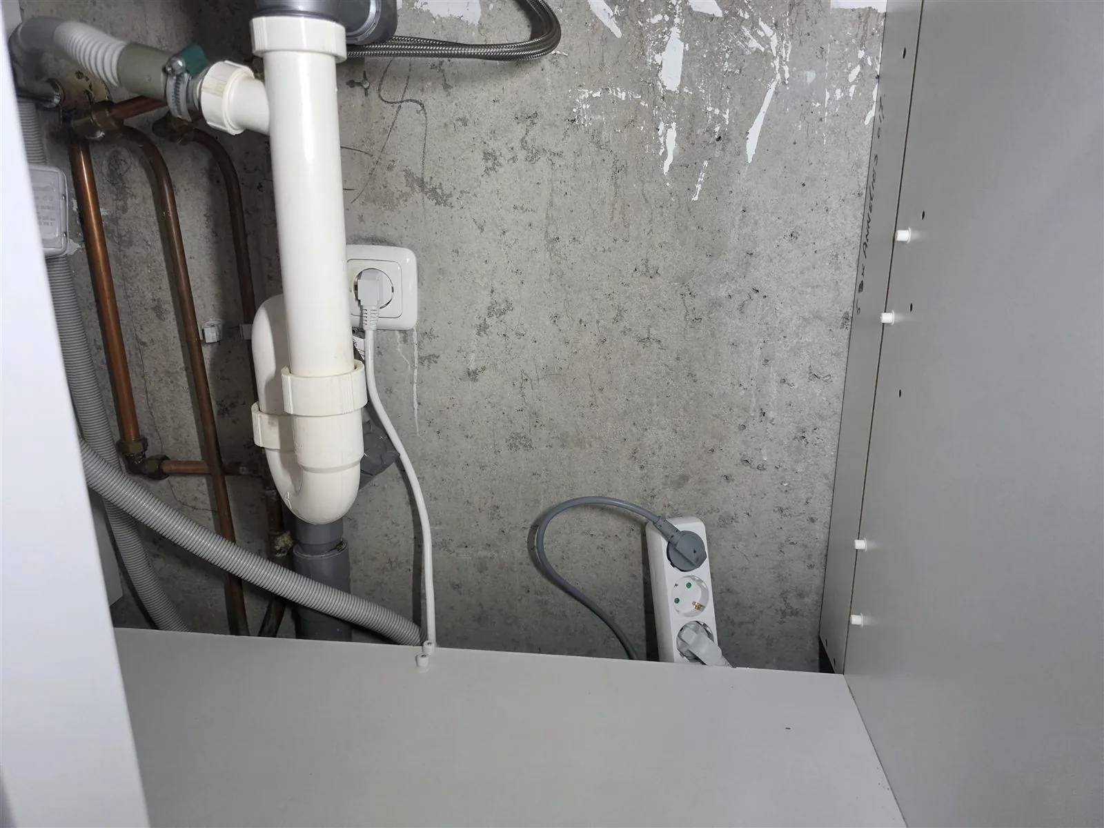 Losse stekkerdoos met oven en vaatwasser op de bodem van het gootsteenkastje, onder de sifon