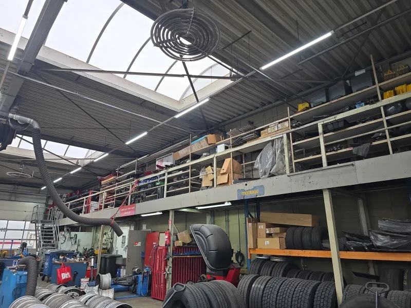 Gesloten led-lijnarmaturen boven de werkzones en open buisarmaturen bij de stellingen in een truckwerkplaats in het Westland