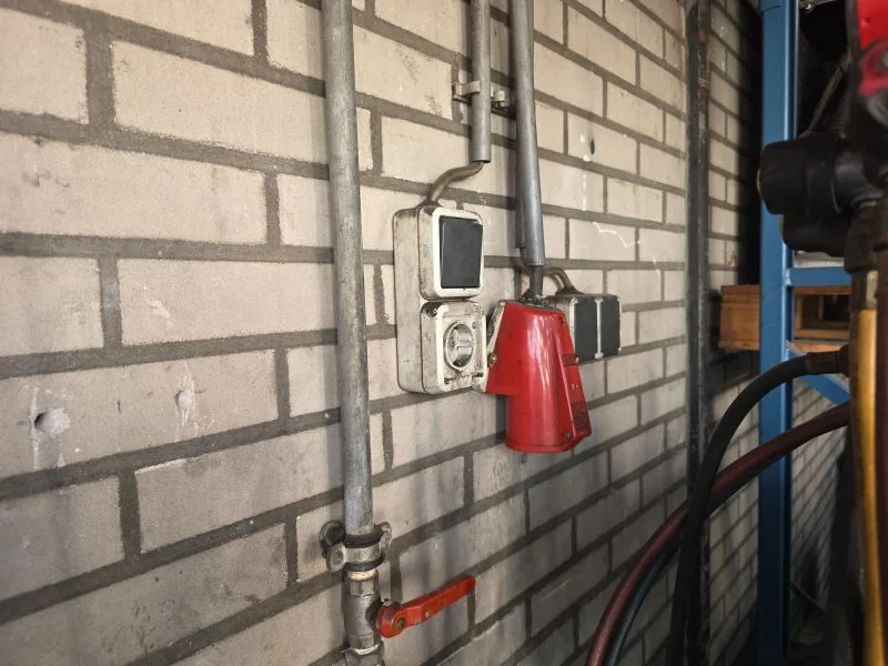 Opbouwcontactdozen aan een muur in een truckwerkplaats, waarbij het veersluitdeksel van een spatwaterdichte contactdoos is afgebroken